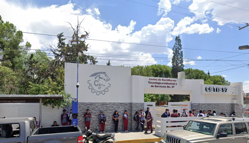 Fotografía en la que se muestra la entrada del plantel, conformada por una reja blanca que da acceso a las instalaciones y dos muros altos de color blanco y gris. Arriba de la reja, en letras de color rojo dice CENTRO DE BACHILLERATO TECNOLÓGICO INDUSTRIAL Y DE SERVICIOS NÚMERO 97.